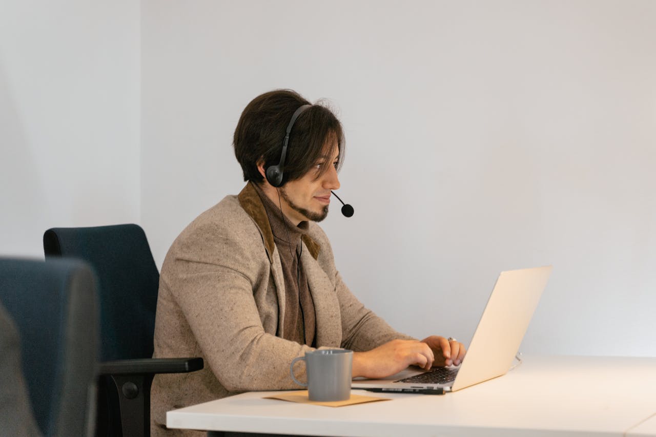 hero-img-02 Man with headset typing on laptop in a modern office setting, providing customer support.